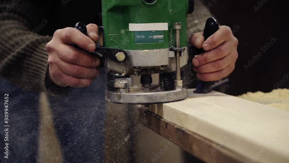 Extremely close up of a craftmans hands working with polishing with manual grinding machine at wood workshop. Grinds a large wooden plank. Dust and chips are scattering on the floor. Unrecognizable Extremely close up of a craftmans hands working with polishing with manual grinding machine at wood workshop. Grinds a large wooden plank. Dust and chips are scattering on the floor. Unrecognizable