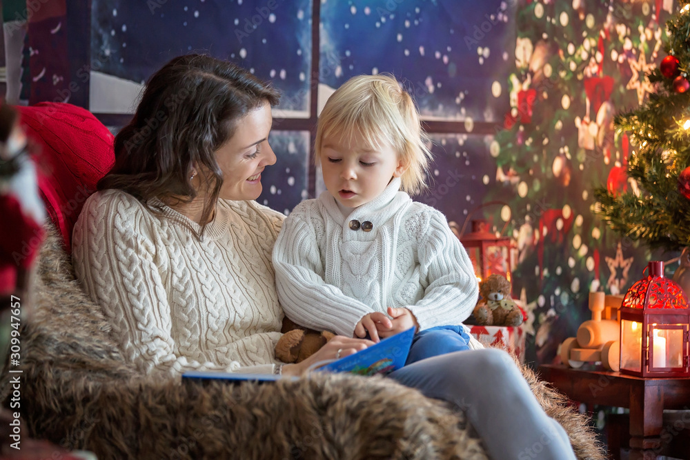 Beautiful young mom and blonde toddler boy, sitting in cozy living romm, decorated for Christmas Beautiful young mom and blonde toddler boy, sitting in cozy living romm, decorated for Christmas