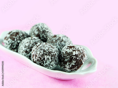 Chocolate rum balls covered with dessicated coconut powder in white porcelain dish