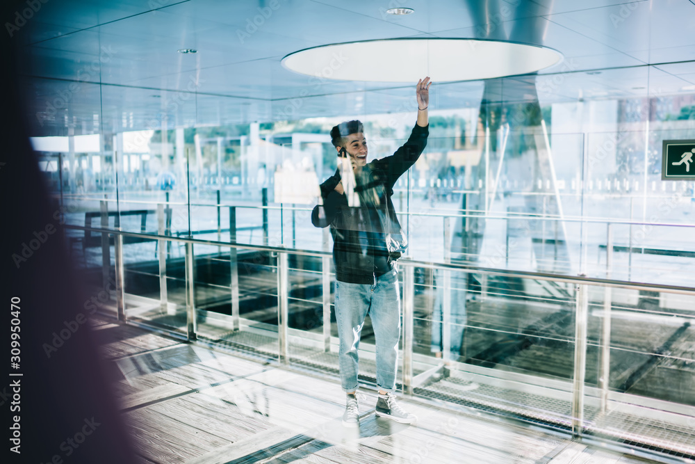 Young male waving hand while having phone call Young male waving hand while having phone call