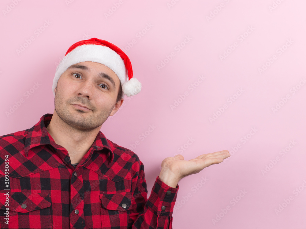 Emotions on the face, smile, joy. A man in a plaid rabbit and a Christmas red hat, on a pink background, copy space. Emotions on the face, smile, joy. A man in a plaid rabbit and a Christmas red hat, on a pink background, copy space.