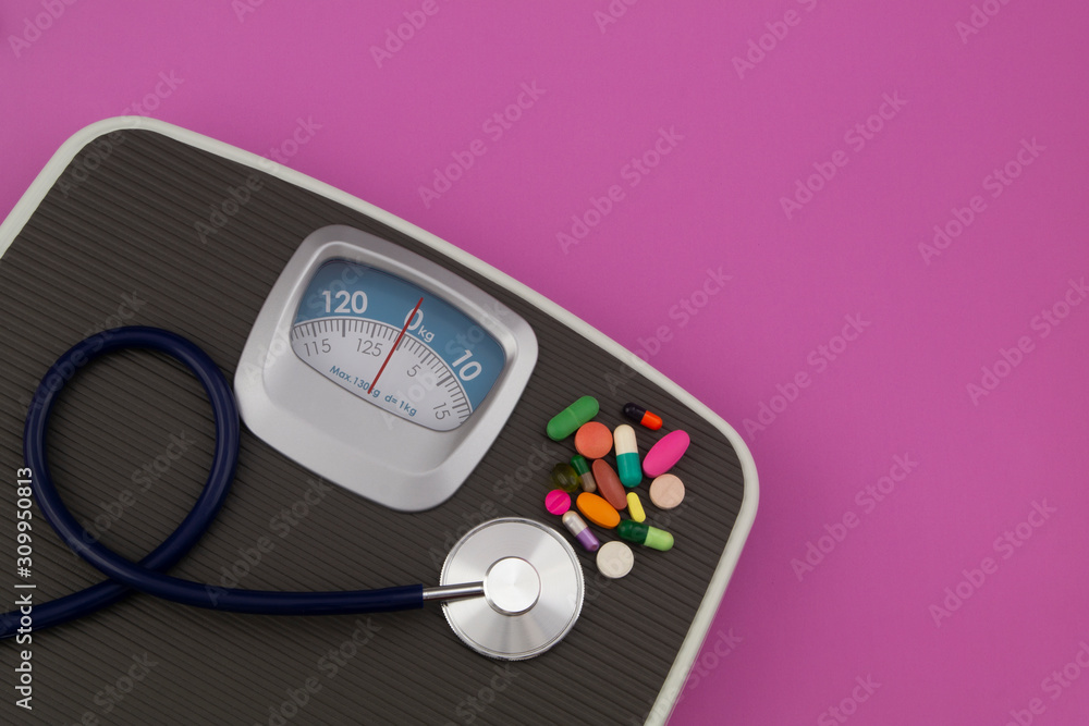 Scale, stethoscope and drugs on pink background with copyspace for text. Loose weight and healthcare concept.