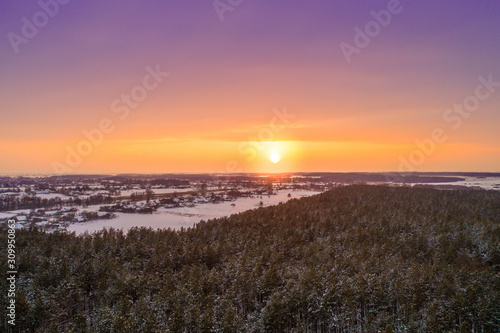 Aerial view of the countryside in the evening. Snowy fields and forest at sunset