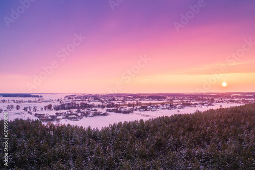 Aerial view of the countryside in the evening. Snowy fields and forest at sunset