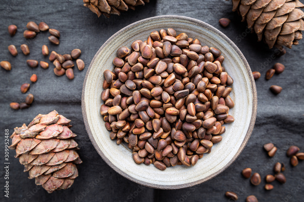 Cedar or pine nuts in a bowl with cones on gray background, top view Cedar or pine nuts in a bowl with cones on gray background, top view