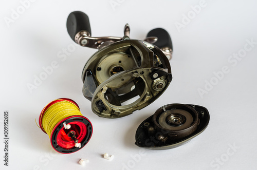 Disassembled Baitcasting Reel. Close-up of fishing tackle on a light background. Housing, spool with cord and centrifugal brake. Repair and service. Selective focus. photo