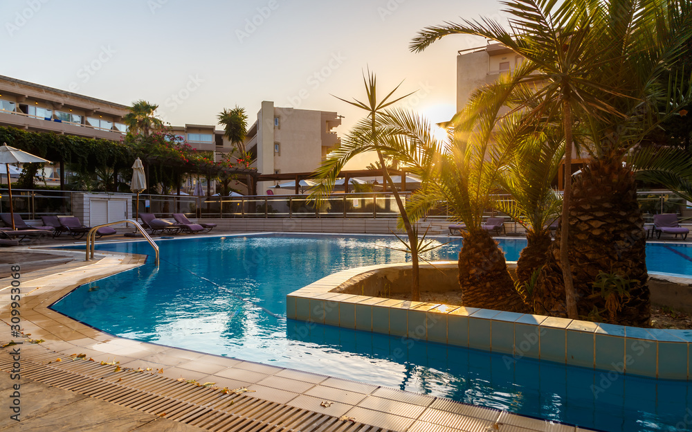 Fototapeta premium Beautiful tropical beach front hotel resort with swimming pool, sun-loungers and palm trees during warm sunny day, paradise destination for vacations