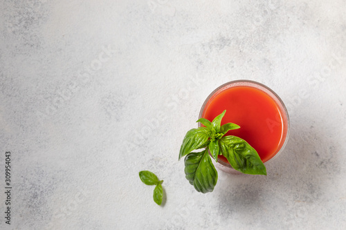 Fresh tomato juice with basil in a glass on a light background.