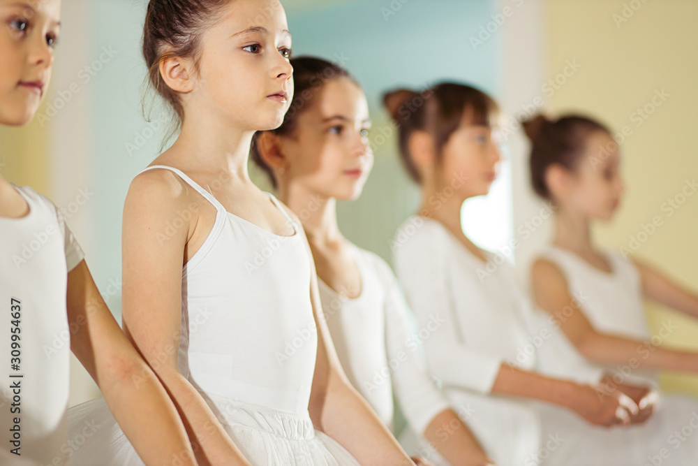Obraz premium group of little caucasian ballerinas stand in a row and practice ballet together. pretty amazing dance performers in studio
