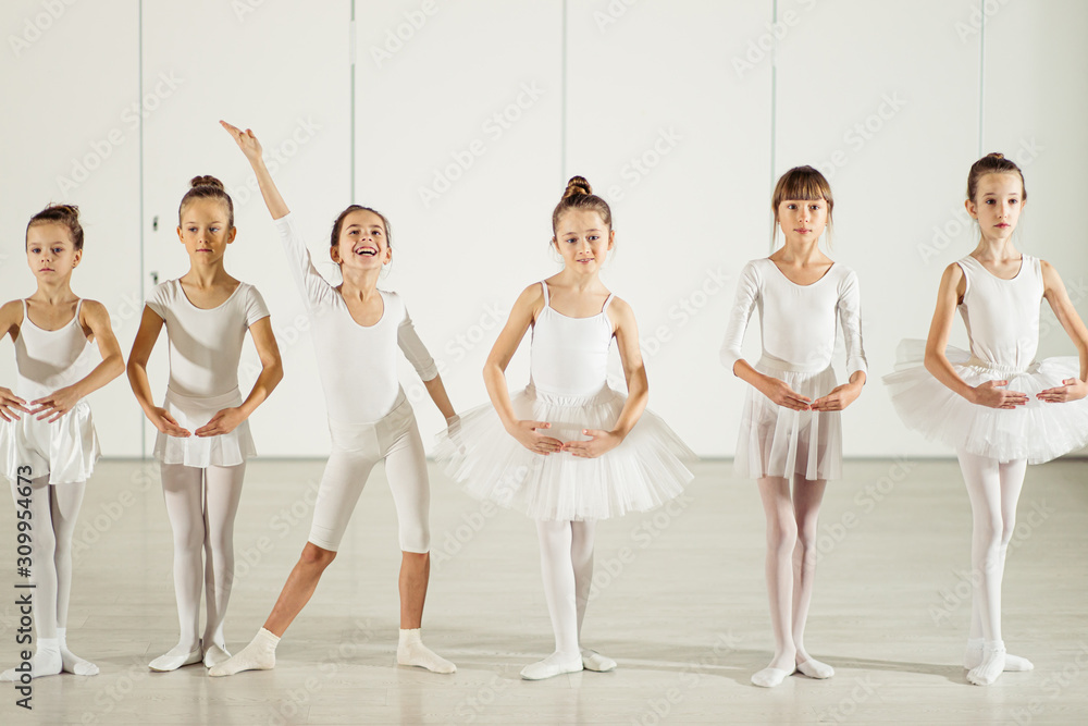 sweet caucasian little girls ballerinas stand in a row in a position wearing white tutu suit, while one girl standing in funny pose, smile, happy ballet group of young girls sweet caucasian little girls ballerinas stand in a row in a position wearing white tutu suit, while one girl standing in funny pose, smile, happy ballet group of young girls