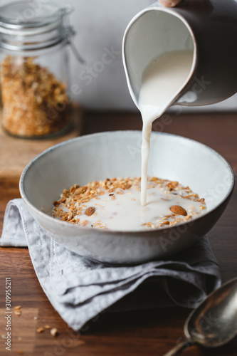 Fotografia Almond milk is poured in a ceramic bowl with baked granola
