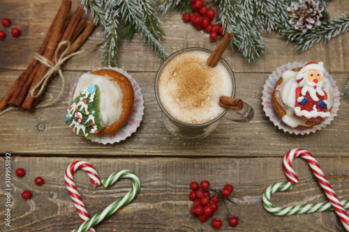 Fototapeta Naklejka Na Ścianę i Meble -  Christmas background with cocoa or hot chocolate, muffin or cupcakes with Santa Claus, snowman and Christmas tree, candy cane, wooden background. Holidays and Christmas concept. Flat lay. Top view.