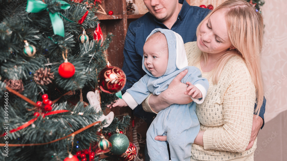 happy parents and their baby standing near the Christmas tree happy parents and their baby standing near the Christmas tree