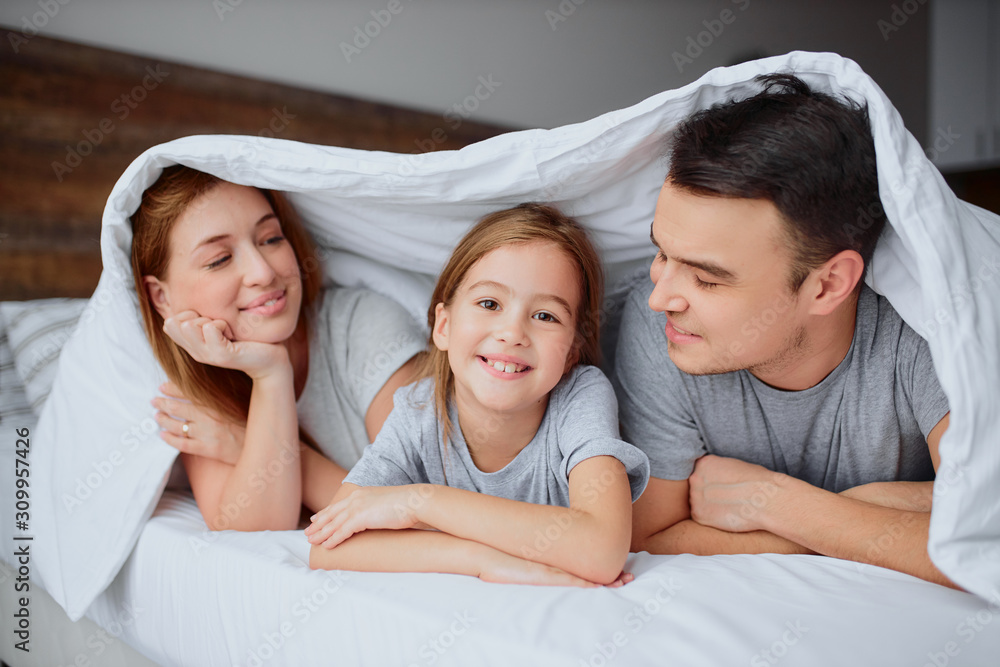 portrait of happy smiling girl with parents together on bed, happy family concept. lying on bed under blanket portrait of happy smiling girl with parents together on bed, happy family concept. lying on bed under blanket