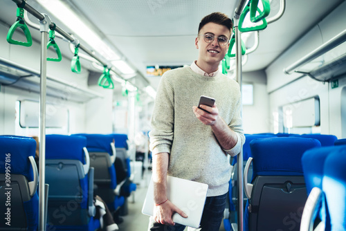 Cheerful man with smartphone standing in train
