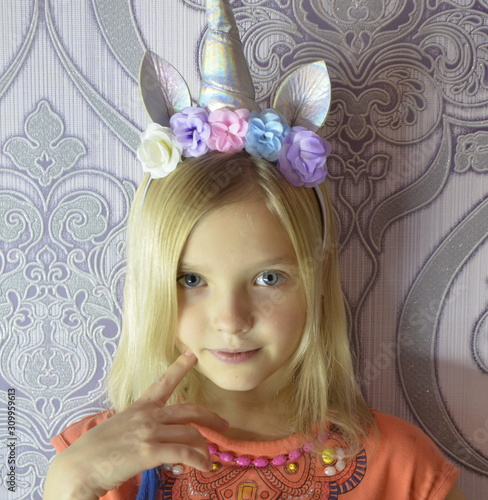 Portrait of a beautiful girl with blue eyes and blond hair. On his head is a wreath of flowers and a unicorn.