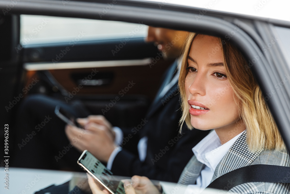 Photo of blonde businesswoman using cellphone while going in car