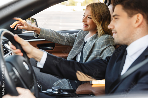 Photo of pleased man and woman talking and smiling while driving in car