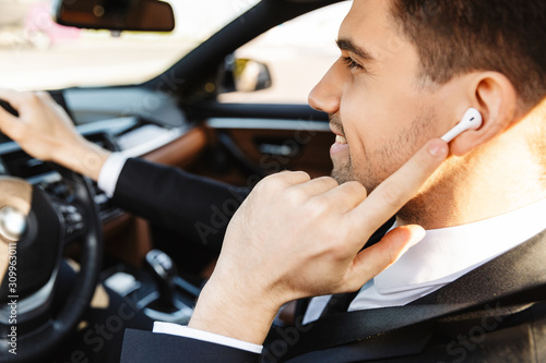 Photo of smiling young businessman using earpod while driving car