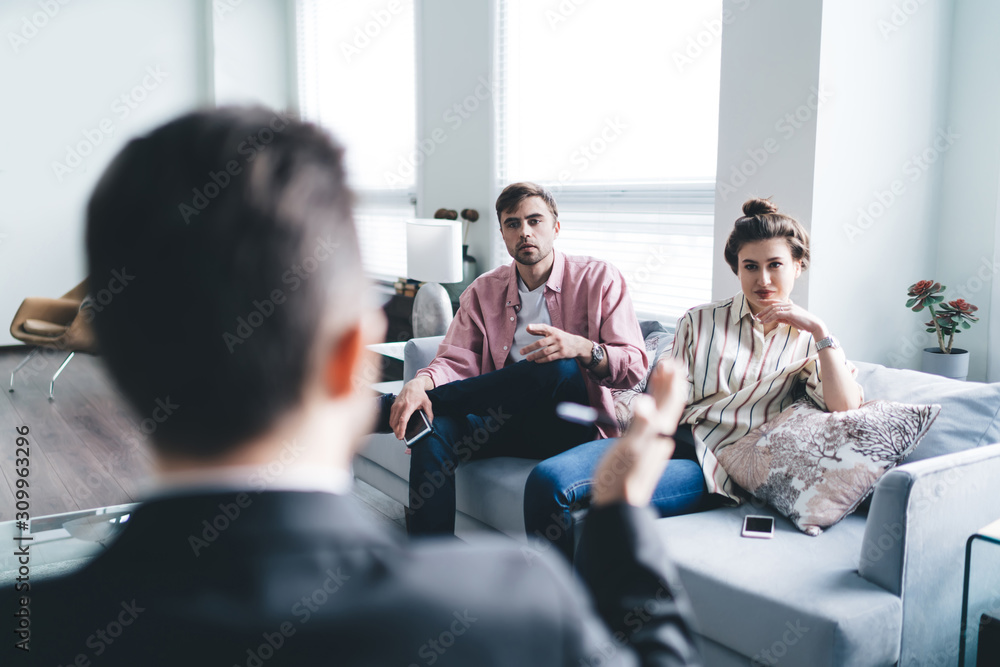 Fototapeta premium Pensive couple sitting on couch and listening to therapist
