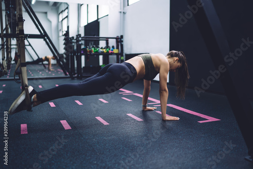 Sportswoman performing fitness exercises with sports loops at gym