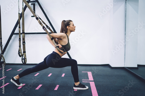 Focused young sportive woman exercising on trx trainer in gym