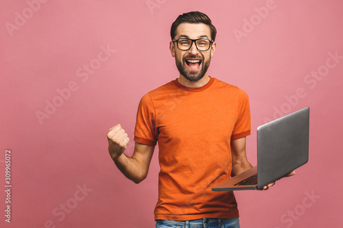 Image of happy excited young man posing isolated over pink background wall using laptop computer make winner gesture. photo