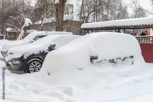 Heavily snowbound cars are standing fixedly in snow in yard house.