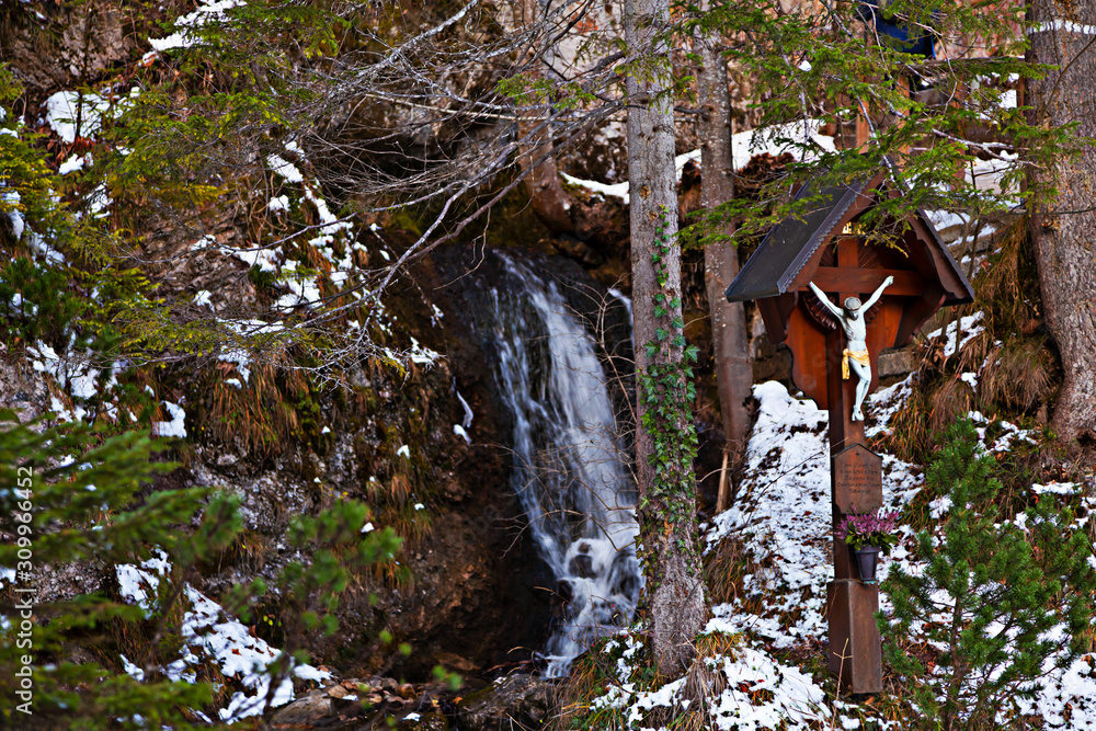 Wegkreuz in Bergtal mit einem Wasserfall im Hintergrund Wegkreuz in Bergtal mit einem Wasserfall im Hintergrund