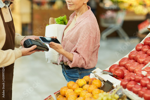 Bild auf Leinwand Cropped portrait of modern woman paying via NFC while grocery shopping at farmer