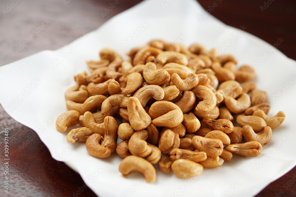 Angle view of fried cashew nuts in a dish with wood table. Angle view of fried cashew nuts in a dish with wood table.