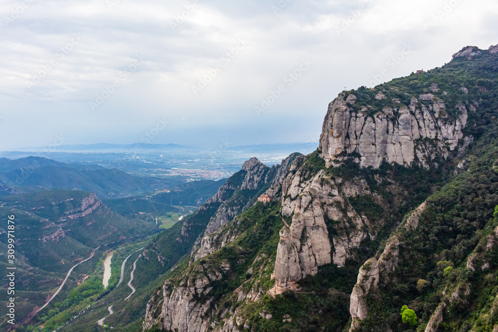 Panoramic view of the mountains of the southern massif with the Hermitage of Cova hanging on its slope, Monistrol de Monserrat, Catalonia, Spain