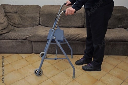 High angle on disabled using a walker at home. Elderly with sneakers walking with the help of a blue walker.