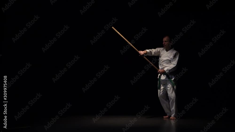 Kendo fighter on white kimono practicing martial art with the bamboo bokken on black background. Slow motion Kendo fighter on white kimono practicing martial art with the bamboo bokken on black background. Slow motion