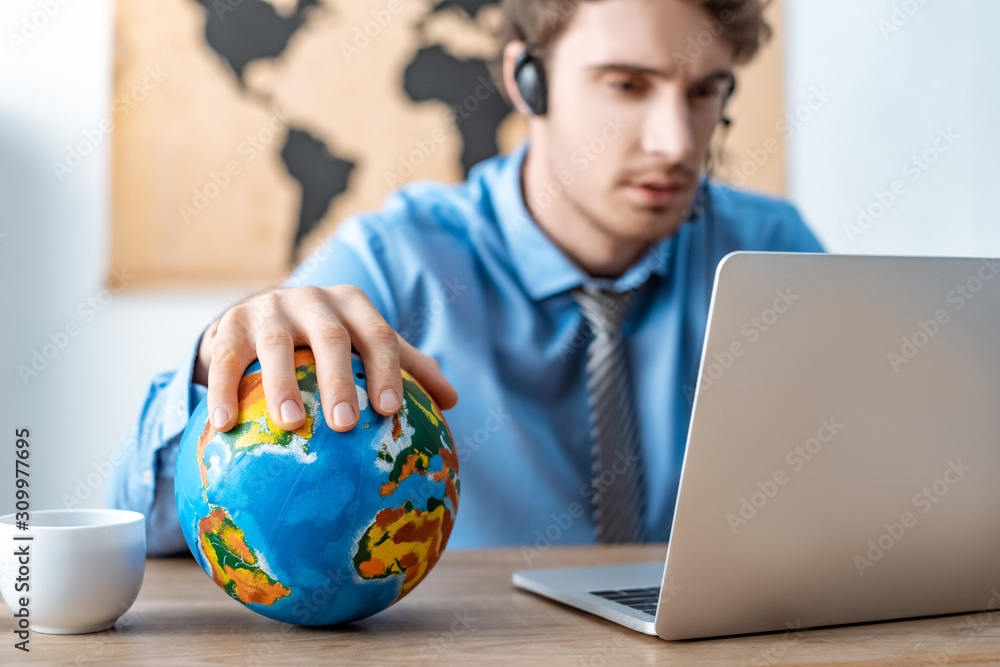selective focus of travel agent touching globe while working near laptop selective focus of travel agent touching globe while working near laptop