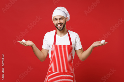 Smiling young bearded male chef cook or baker man in striped apron white t-shirt toque chefs hat isolated on red background in studio. Cooking food concept. Mock up copy space. Holding eggs in hands.