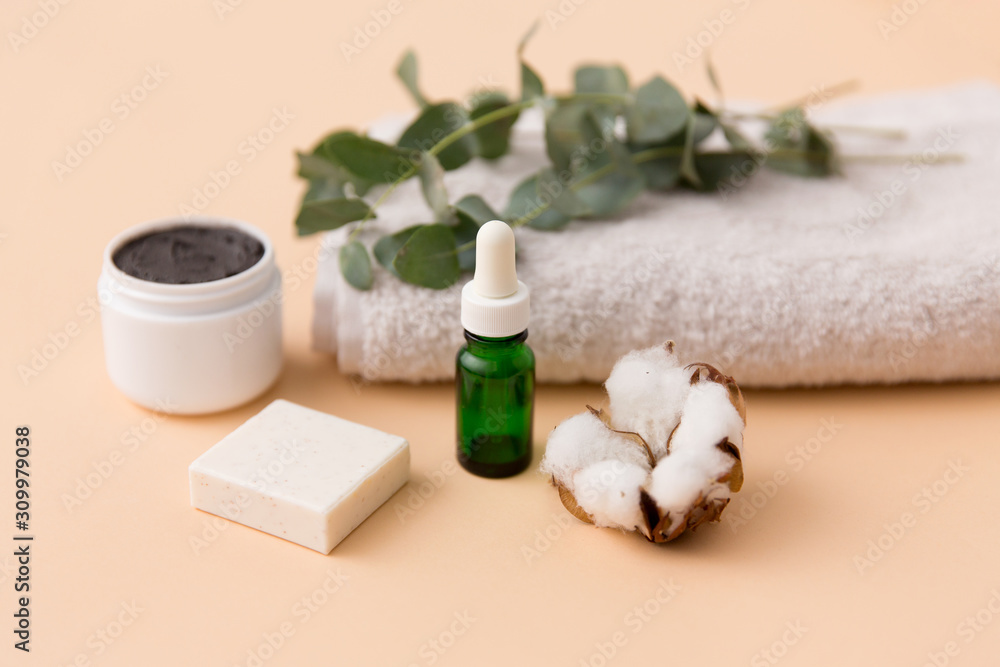 beauty and spa concept - serum or essential oil, mask, soap bar, eucalyptus cinerea and cotton flower on bath towel