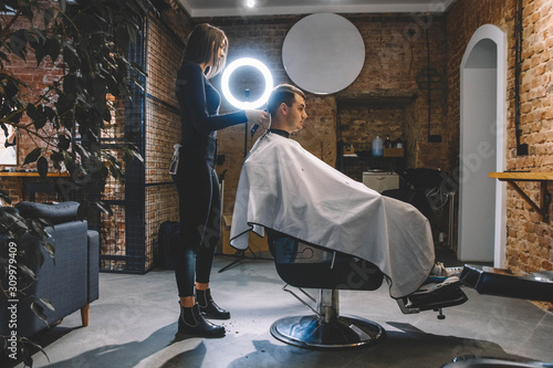 Beautiful female hairdresser shaves the head of a client sitting in a chair with an electric trimmer in a barber shop. Concept of advertising and hairdressing