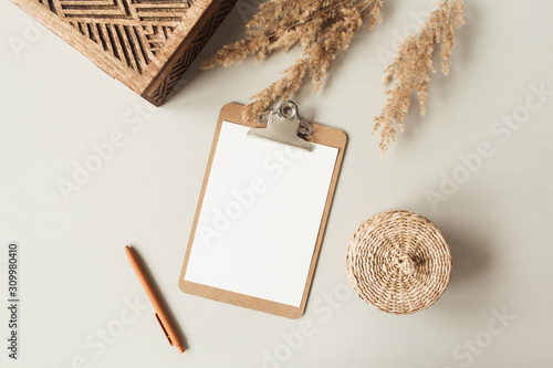 Blank sheet clipboard with empty copy space, pen, rattan casket on neutral background. Flat lay, top view minimal business template for social media, magazine, blog. Home office desk table workspace.