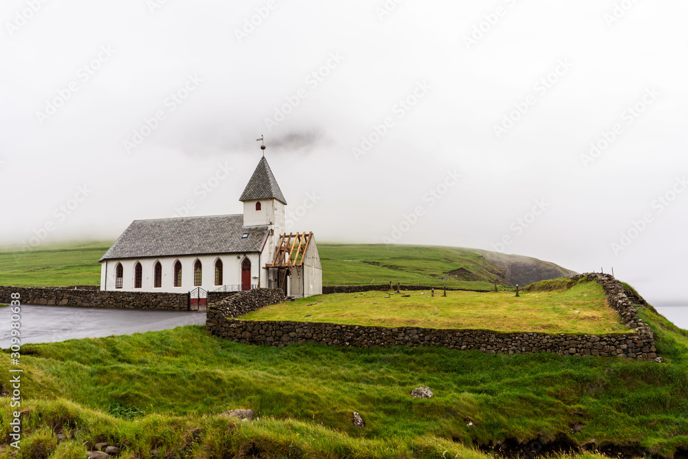 Traditional Faroese wooden church surrounded with green hills, overcast sky on horizon. Faroe Islands, Denmark. Traditional Faroese wooden church surrounded with green hills, overcast sky on horizon. Faroe Islands, Denmark.