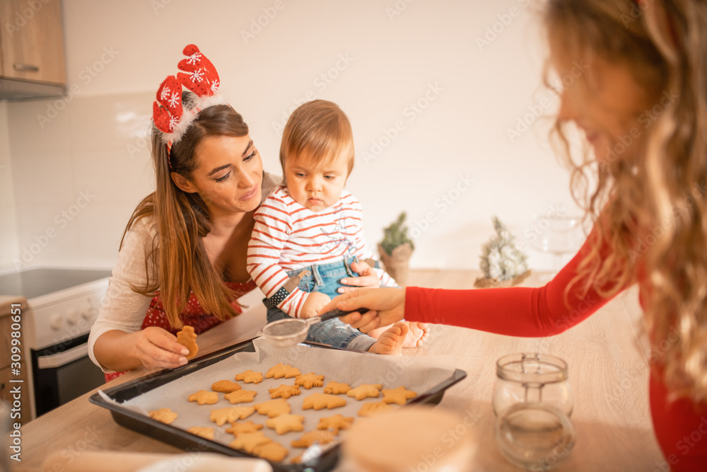 Fototapeta premium A baby, mom and aunt preparing Christmas cookies in the kitchen.