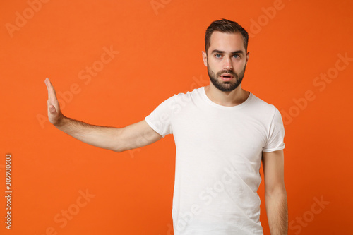 Young man in casual white t-shirt posing isolated on bright orange wall background studio portrait. People sincere emotions lifestyle concept. Mock up copy space. Showing stop gesture aside with palm.