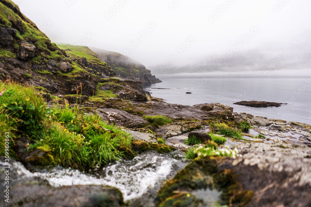 Water stream flowing into the ocean in Vidareidi village, Faroe Islands. Great overcast sky and green hills. Water stream flowing into the ocean in Vidareidi village, Faroe Islands. Great overcast sky and green hills.