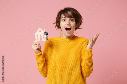 Shocked young brunette woman girl in yellow sweater posing isolated on pastel pink background studio portrait. People lifestyle concept. Mock up copy space. Hold house bunch of keys, spreading hands.