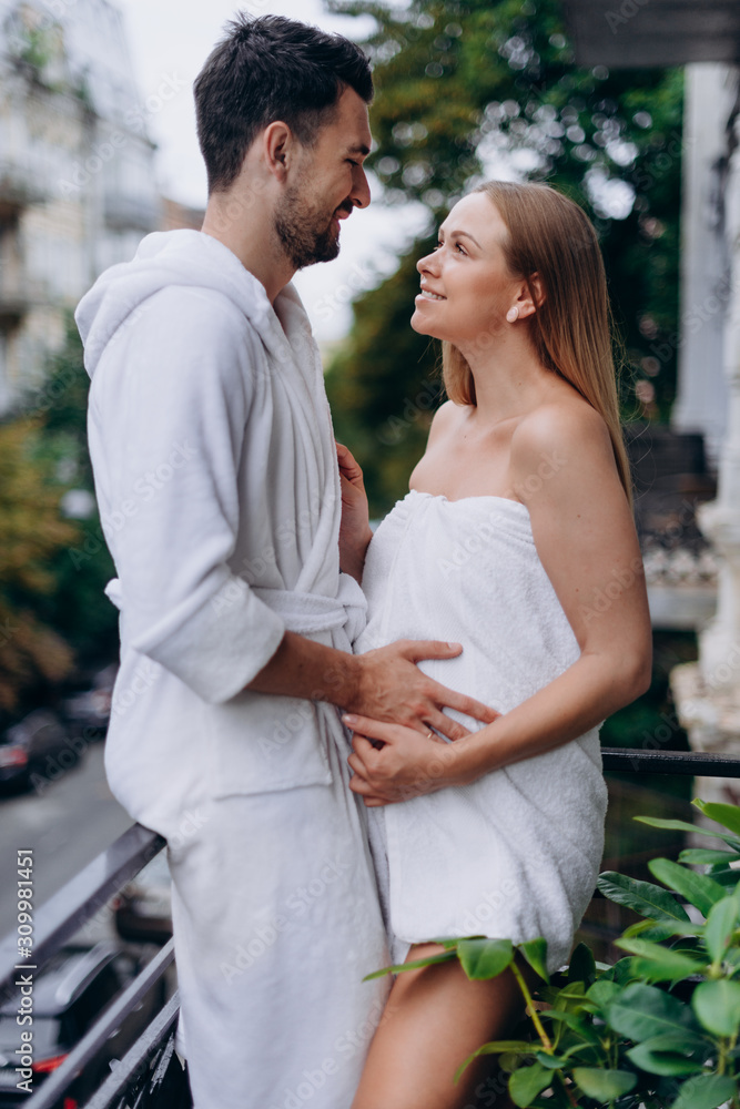 Pregnant woman wrapped in towel on balcony with husband Pregnant woman wrapped in towel on balcony with husband
