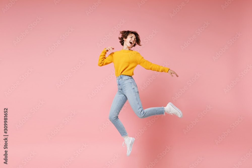 Funny young brunette woman girl in yellow sweater posing isolated on pastel pink background in studio. People lifestyle concept. Mock up copy space. Having fun fooling around, looking aside, jumping.