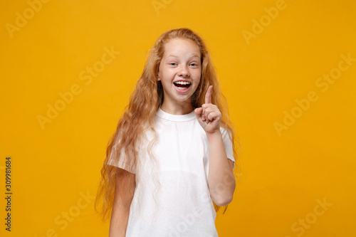 Excited little ginger kid girl 12-13 years old in white t-shirt isolated on yellow background children portrait. Childhood lifestyle concept. Mock up copy space. Hold index finger up with great idea.