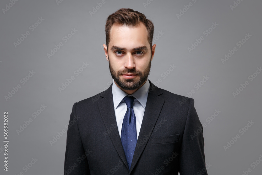 Confident young bearded business man in classic black suit shirt tie posing isolated on grey background studio portrait. Achievement career wealth business concept. Mock up copy space. Looking camera. Confident young bearded business man in classic black suit shirt tie posing isolated on grey background studio portrait. Achievement career wealth business concept. Mock up copy space. Looking camera.