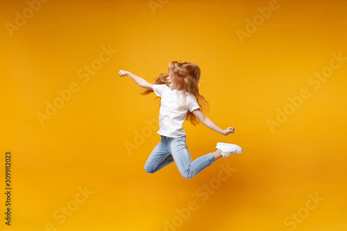Side view of little ginger kid girl 12-13 years old in white t-shirt isolated on yellow background children portrait. Childhood lifestyle concept. Mock up copy space. Having fun, fooling around, jump. © ViDi Studio