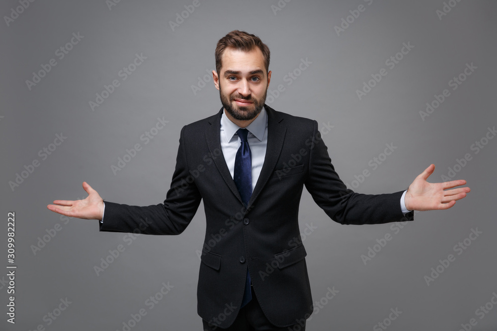 Confused young bearded business man in classic black suit shirt tie posing isolated on grey background. Achievement career wealth business concept. Mock up copy space. Spreading pointing hands aside. Confused young bearded business man in classic black suit shirt tie posing isolated on grey background. Achievement career wealth business concept. Mock up copy space. Spreading pointing hands aside.